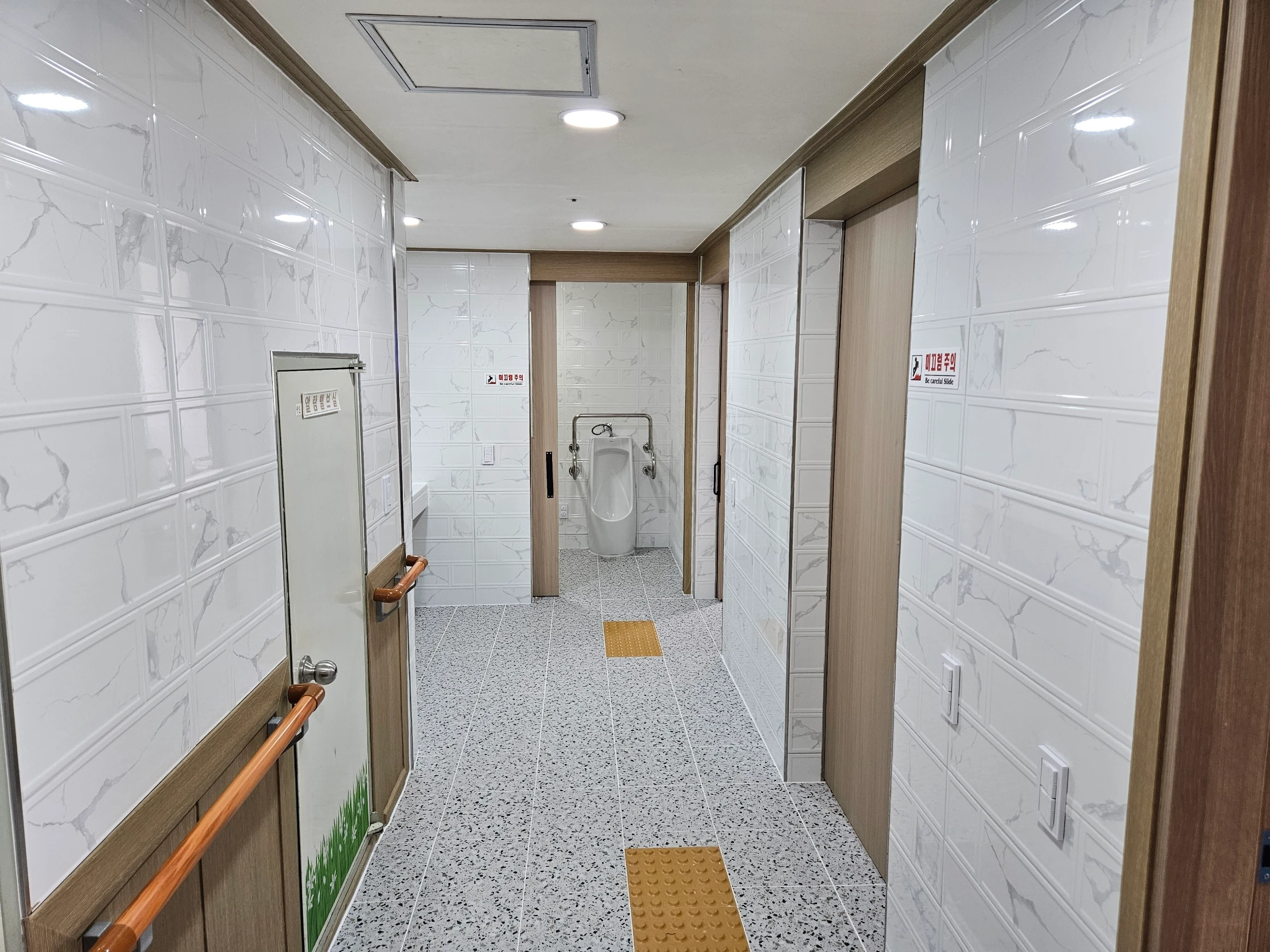 살균소독과 미끄럼주의 문구, 안전 손잡이가 보이는 화장실 접근 공간